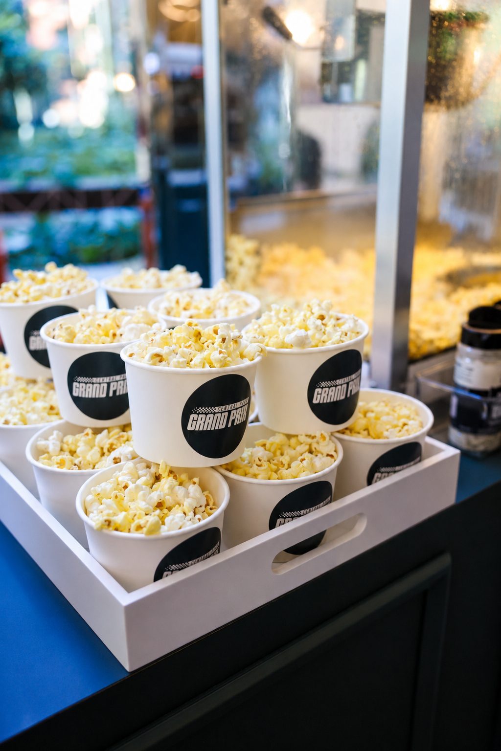 Branded popcorn cups on a serving tray beside a popcorn machine at a corporate event
