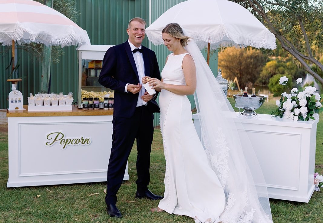 Bride and groom sharing popcorn between Popcorn and Drinks carts with fringed parasols